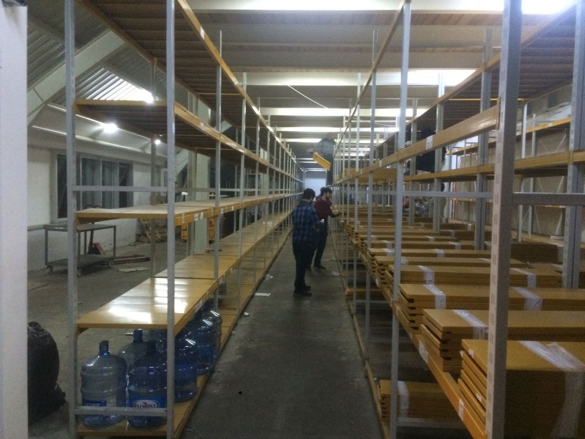 Sunta tablalı ikinci el hafif yük rafı sıralarının arasından uzanan çalışma koridoru