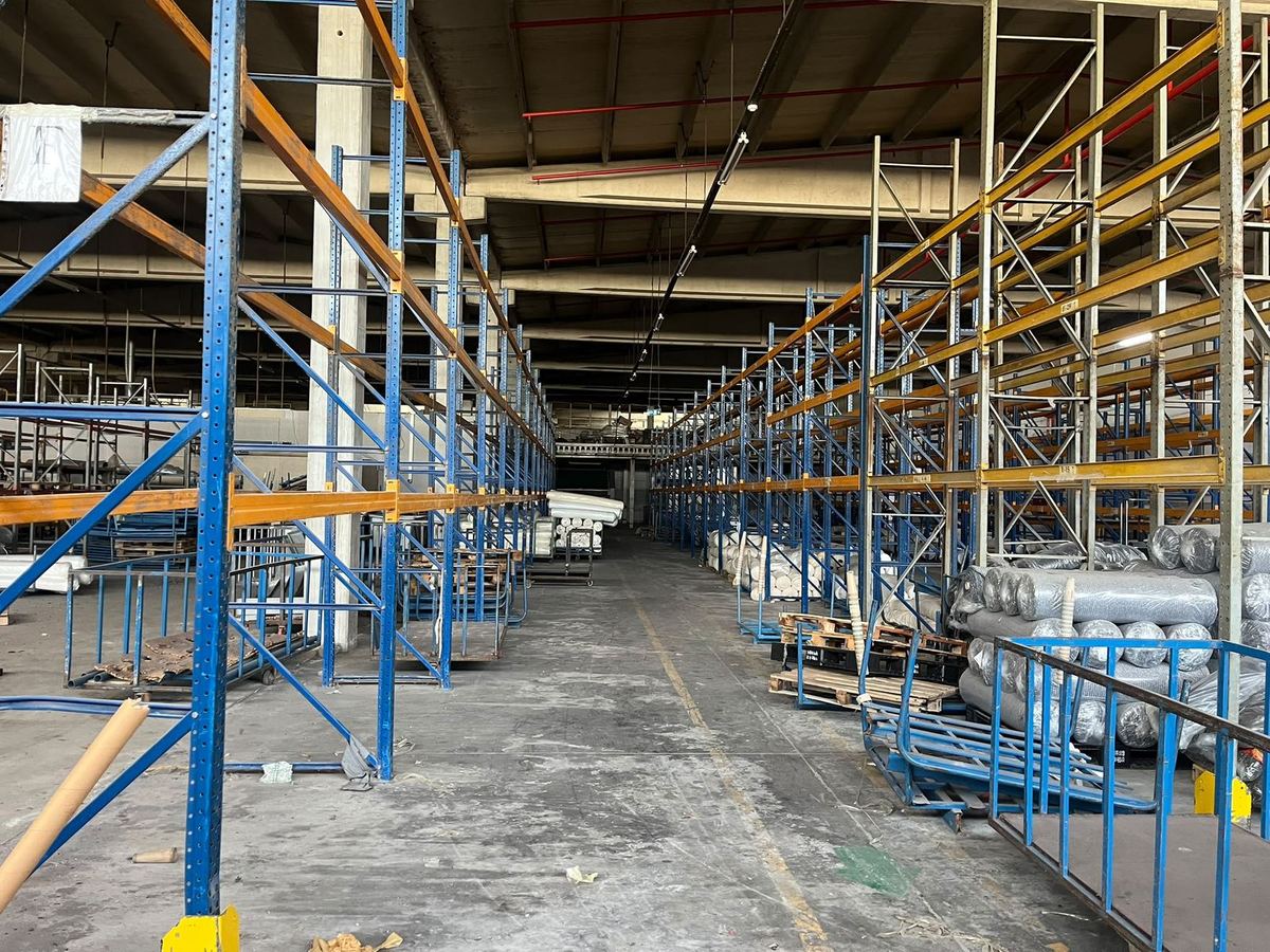 Tekstil topları ve paletlerle dolu bir depoda ikinci el raflarla kurulmuş ana koridor