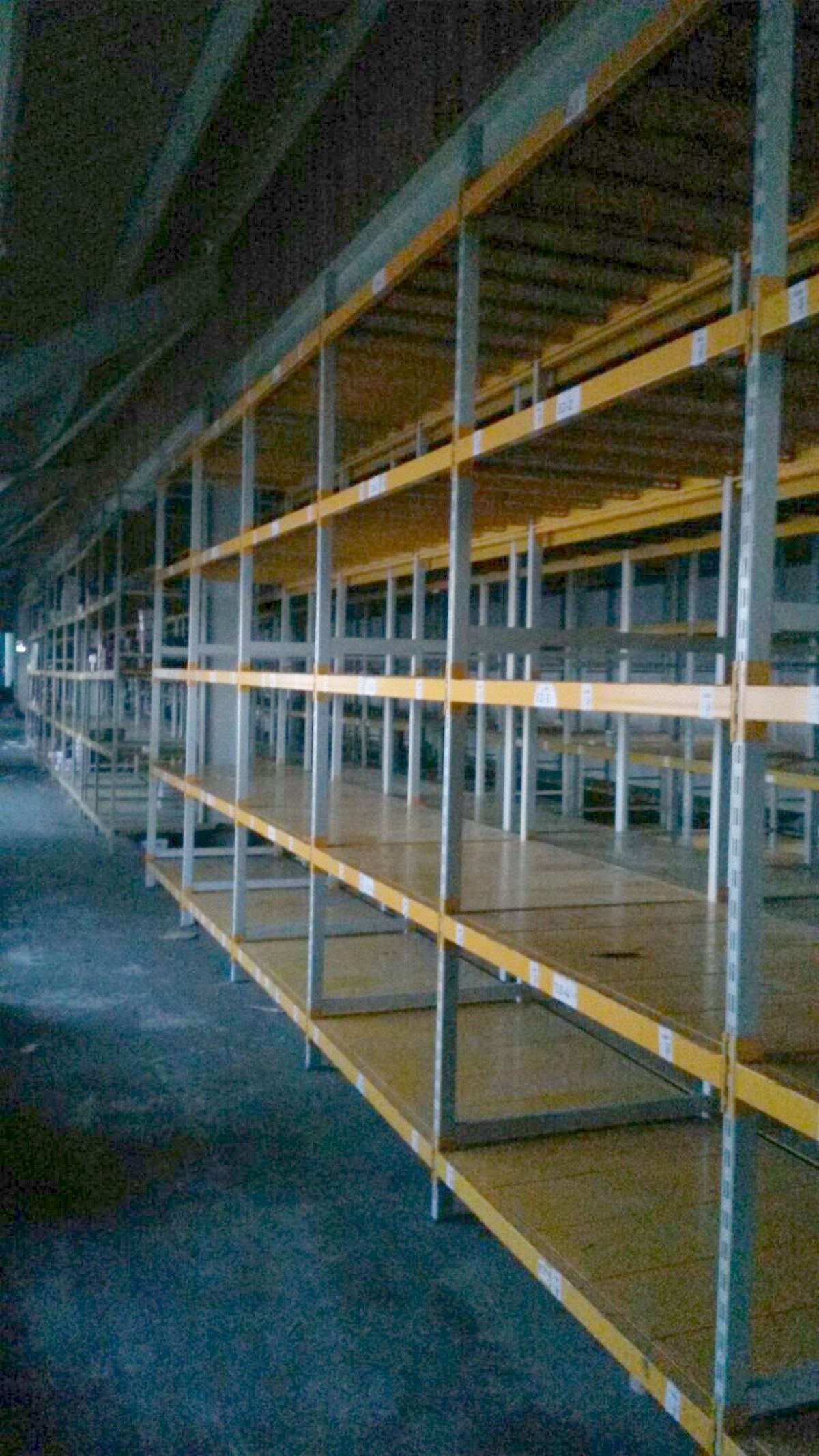 Boşaltılmış bir depoda sarı traversli, ahşap tablalı ikinci el hafif yük rafı hattı