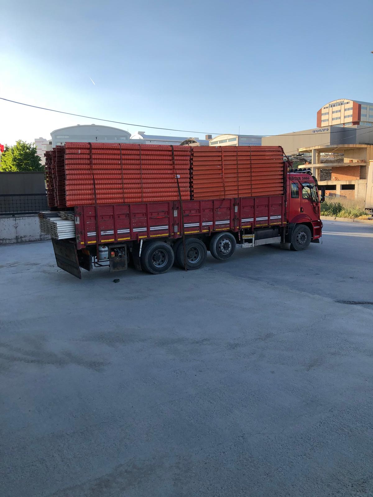 Sökülmüş turuncu raf traverslerinin istiflenerek yüklendiği kırmızı kamyon, depo çıkışında